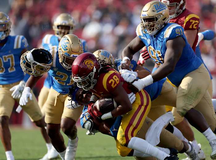 Keaontay Ingram #28 of the USC Trojans rushes as he is tackled by Mitchell Agude #45 of the UCLA Bruins, losing his helmet, during the first quarter at Los Angeles Memorial Coliseum on November 20, 2021 in Los Angeles, California.